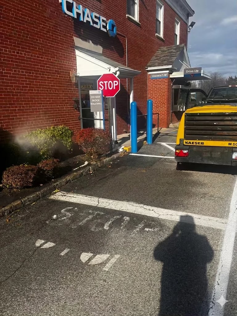 Exterior of Chase Bank branch with red brick building, blue bollards at entrance, yellow truck parked outside, and STOP sign visible